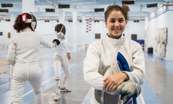 Escrimeuse souriante avec un match d'escrime en arrière-plan
